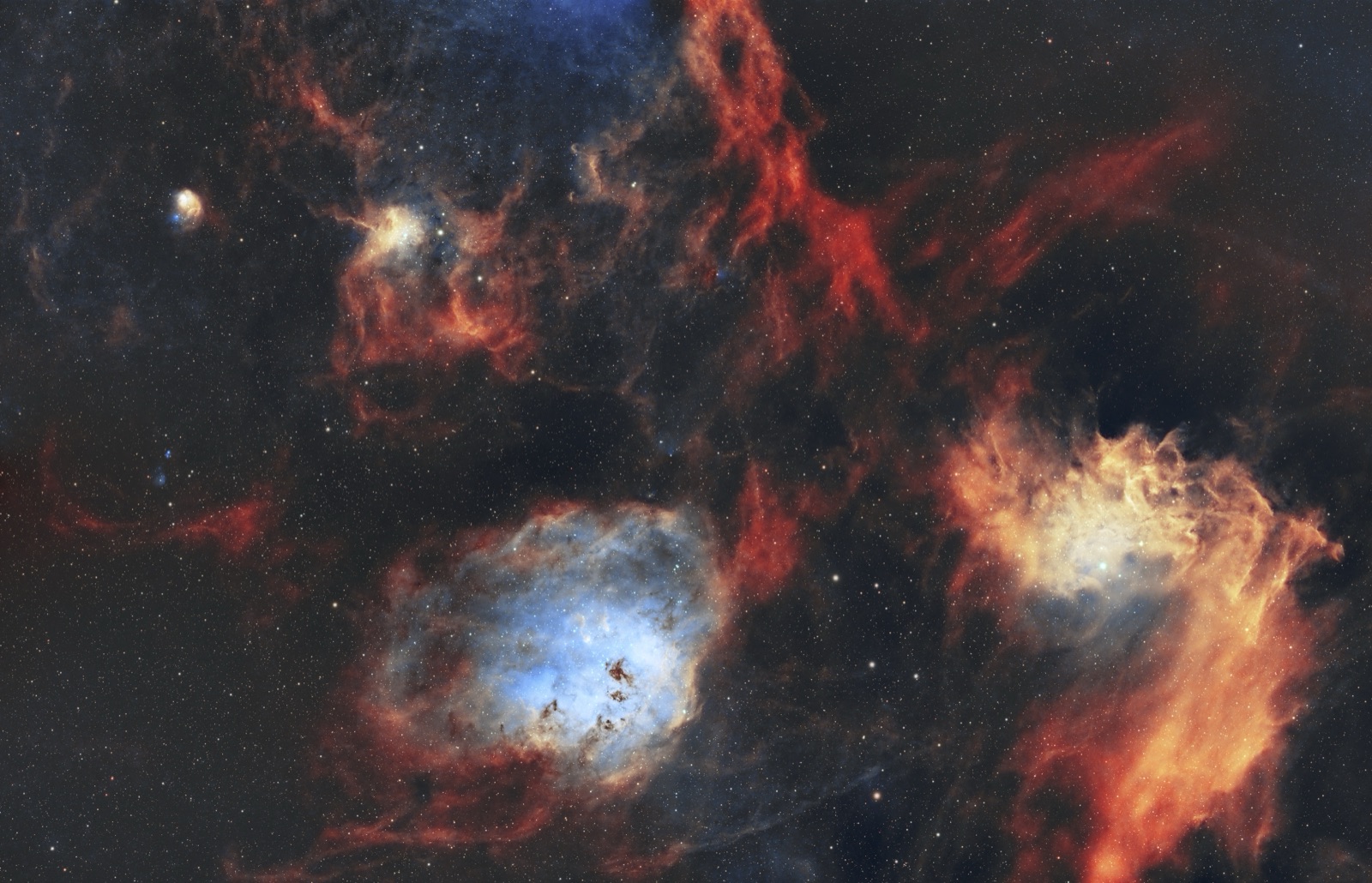 A wide-field view of glowing emission nebulae in blue and gold against a dense star field, rendered in the Hubble palette.